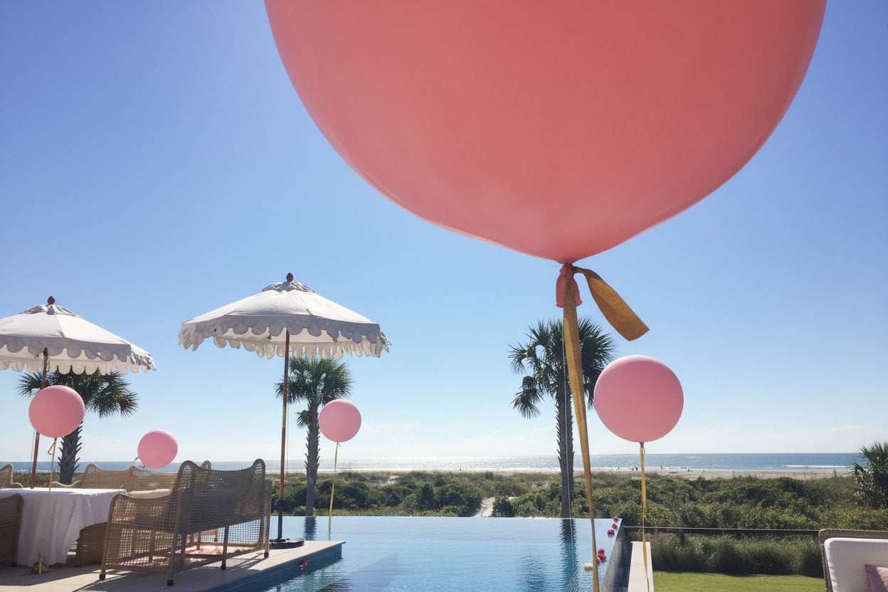 Large pink balloons floating above a pool with palm trees in the background.