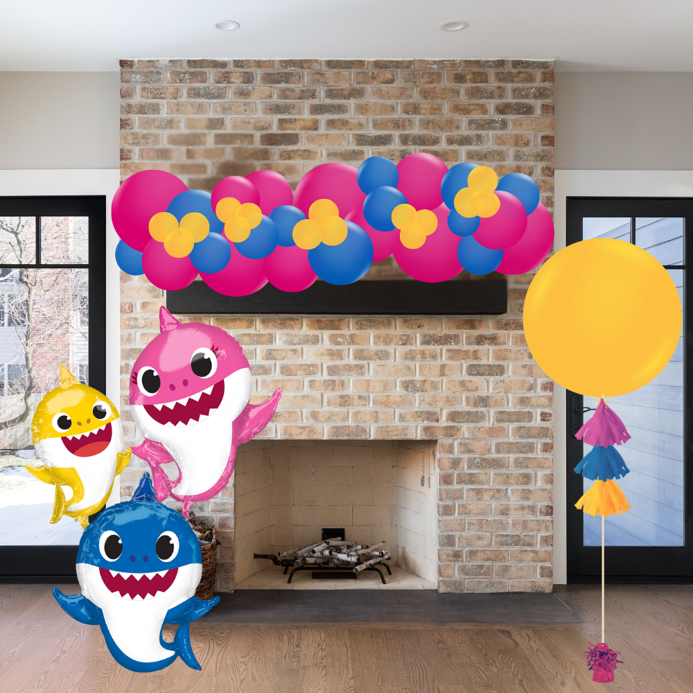 Decorative setup with cartoon shark balloons and colorful balloons in front of a brick fireplace.