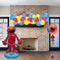 Decorative setup with Elmo balloon and figure in front of a brick fireplace.