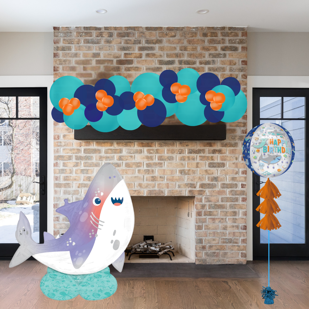 Decorative shark balloon and birthday balloons in front of a brick fireplace.